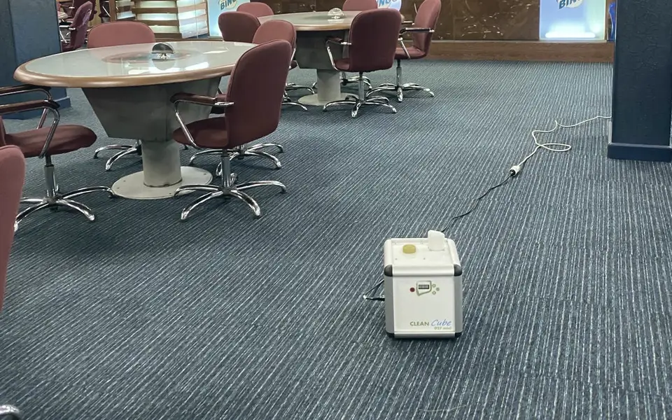 Una sala con tavoli e sedie vuota e l’atomizzatore posato sulla moquette, con il cavo collegato