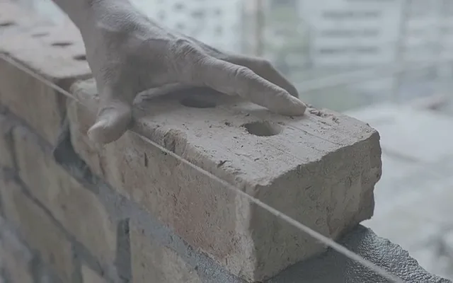 Mano che posa un mattone su un muro in costruzione
