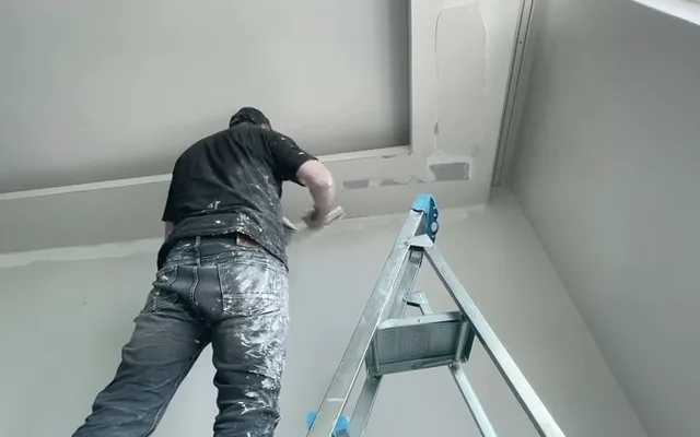 Operaio su una scala che lavora al soffitto di una stanza